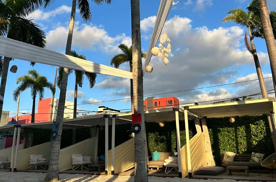 The cabana row at ground level: white pergolas, curtains, sofas and the green wall behind
